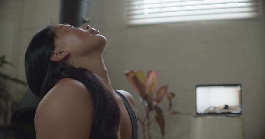 A woman leans her head back while doing yoga as a yoga video plays on her laptop