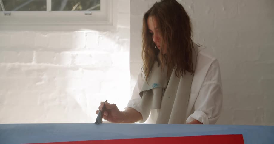 Woman with a towel around her neck uses a paint brush to paint something blue