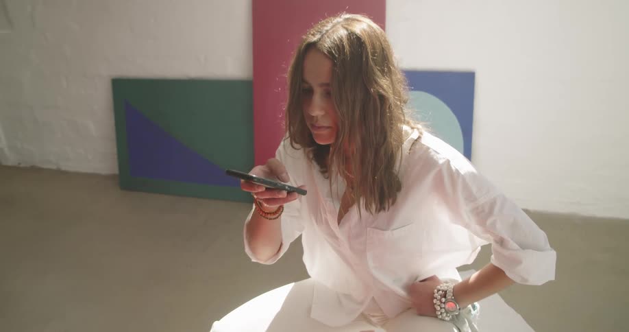 A painter crouches on the ground as she takes a photo of a large canvas on the ground
