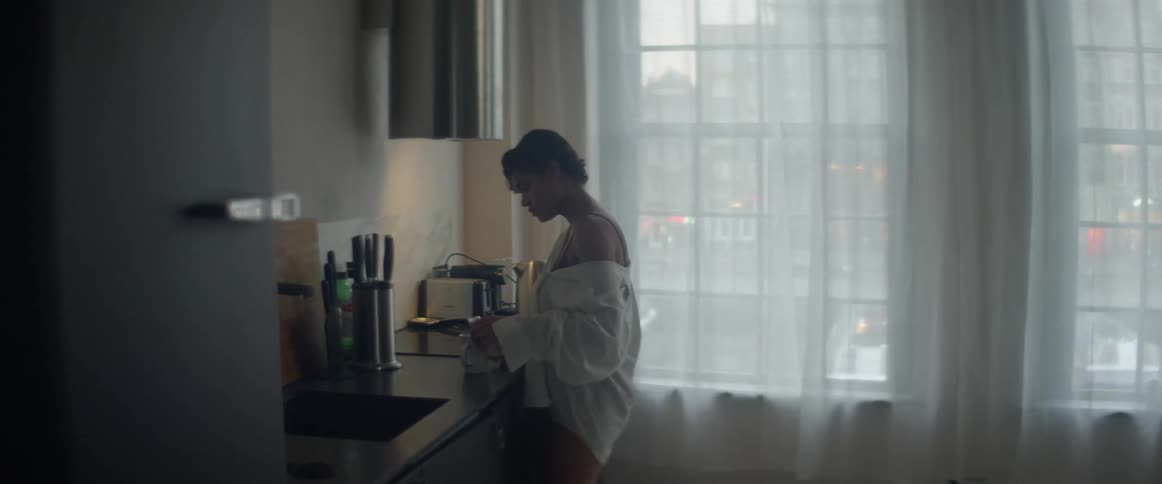 A woman in a kitchen pouring liquid into a mug with windows in the background