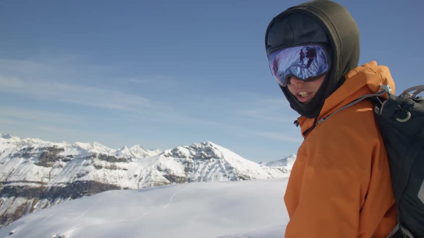 Person wearing cold weather gear and skis stands on snow covered slope looking out toward mountain