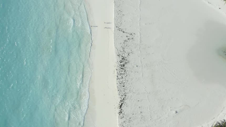 Birds eye view of waves gently lapping on shoreline on sandy beach