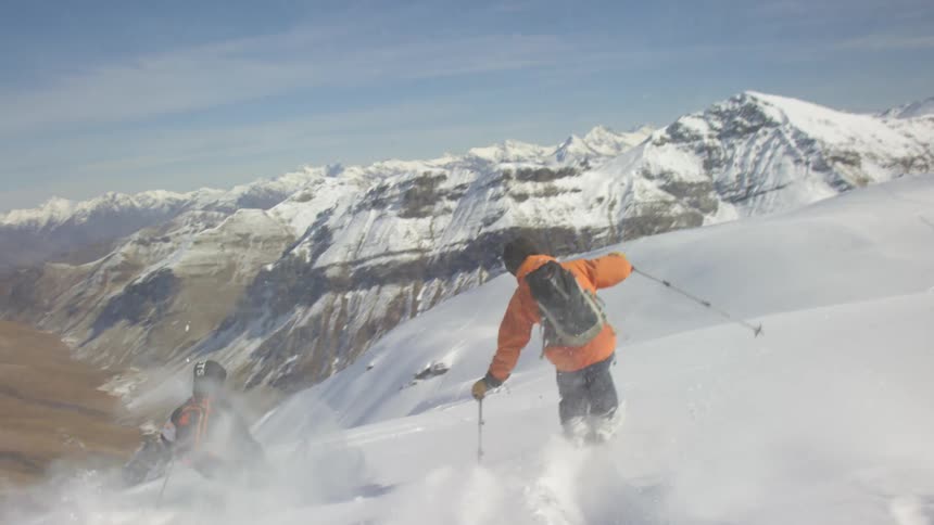 Two people skiing down the snow covered slopes of a mountain range