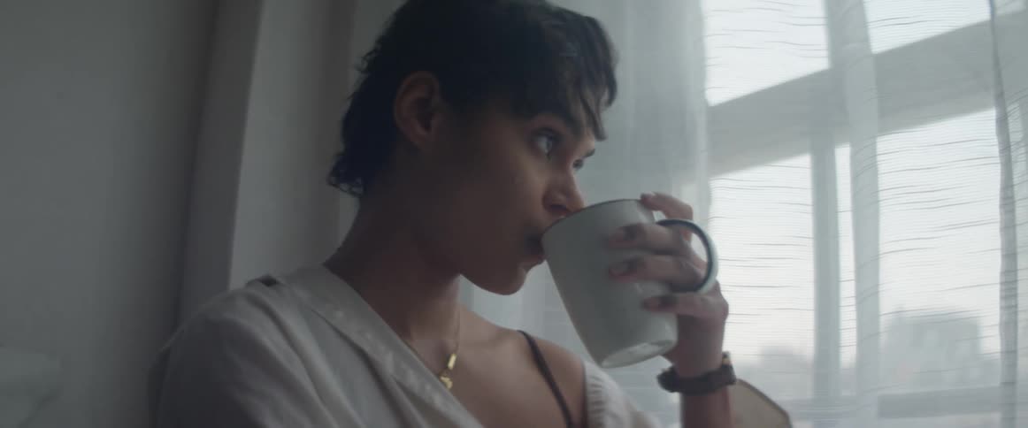 Woman drinking coffee while looking outside through her window