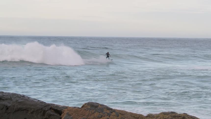 Surfer rides a wave in as water splashes behind him