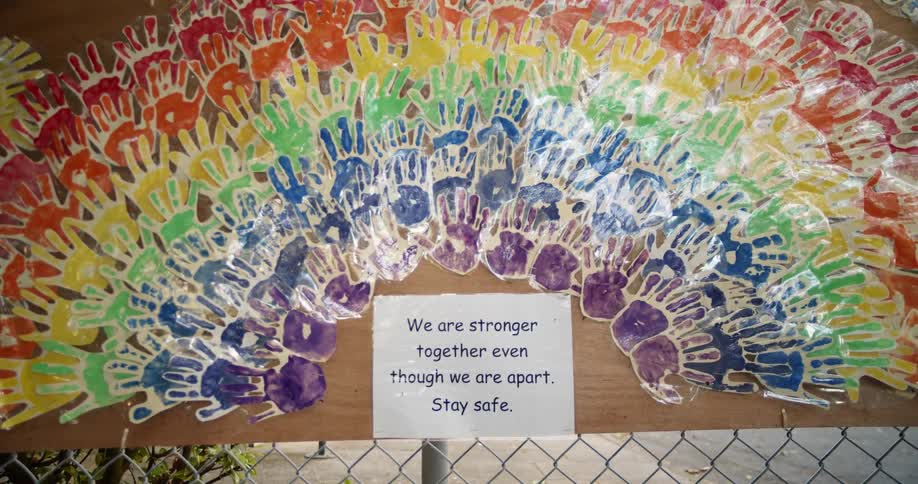 A sign about togetherness sits below a rainbow design made up of handprints dipped in paint