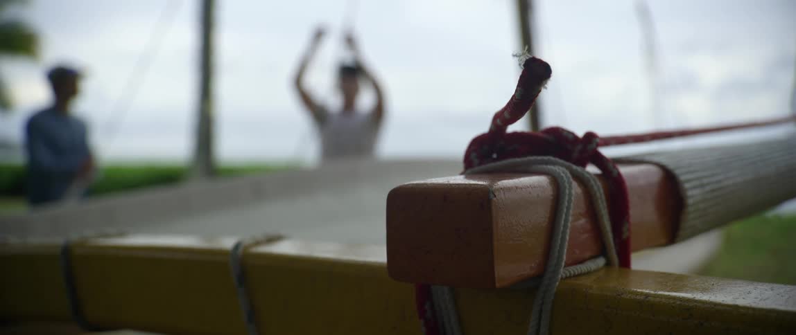 A close up of a piece of wood while two men work on a rope out of focus