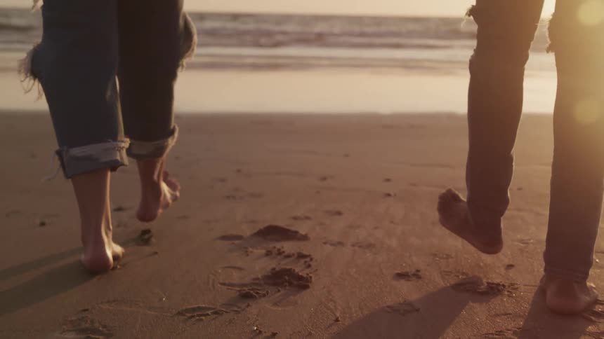 A woman and woman walk on the beach toward the ocean at sunset