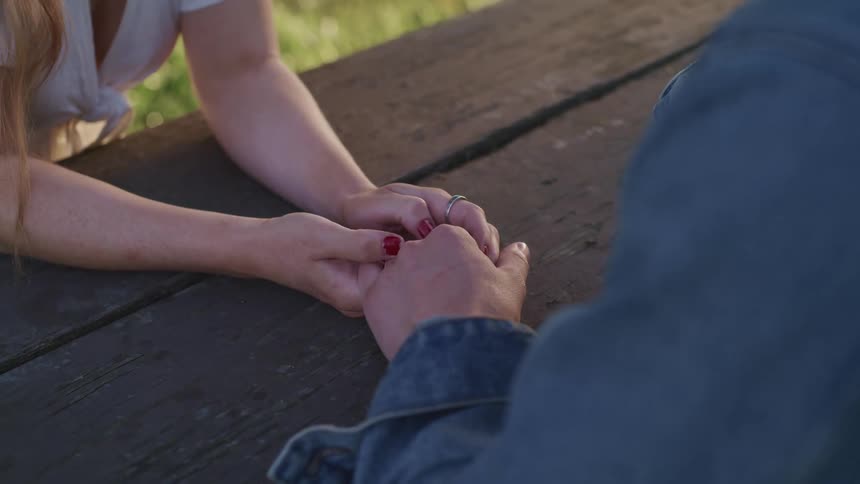 Two people hold hands at the table outside