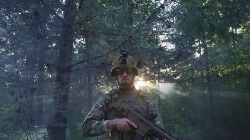 A man is standing in military clothing while holding a gun in a forest