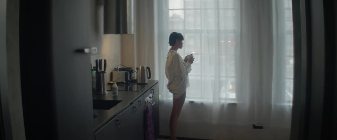 Woman drinking coffee while standing next to her window and looking outside