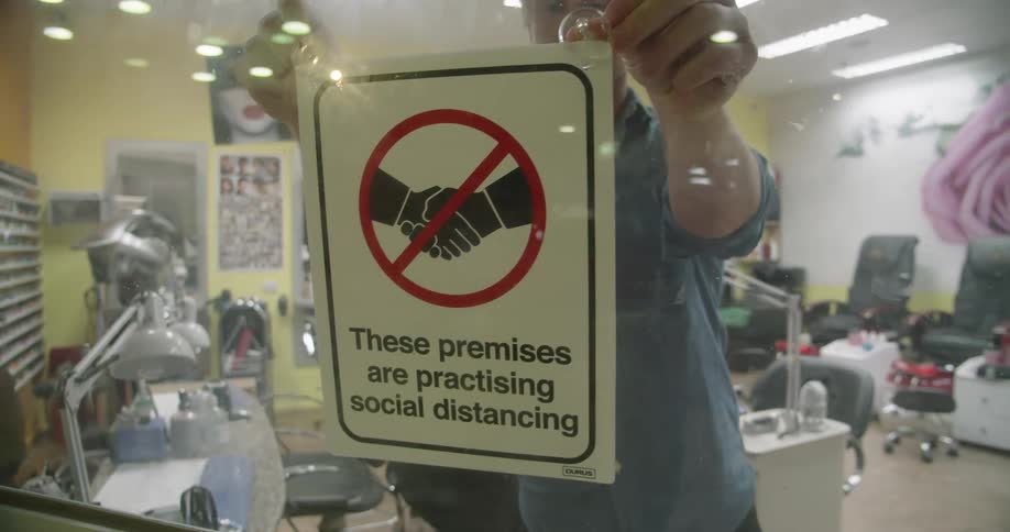 Store owner places a social distancing sign on the window of a hair saloon