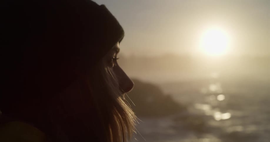 Young long haired woman wearing a beanie looking at the sunrise over the ocean