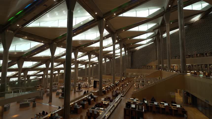 People sit at tables or wander through larger library building with skylights