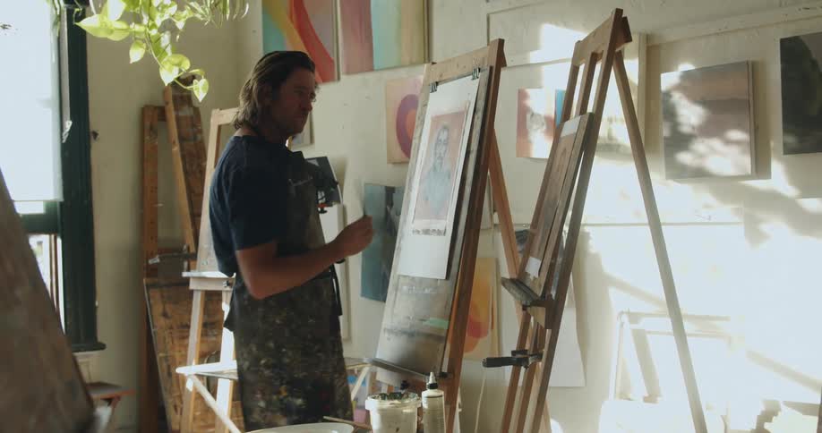 Painter painting with oil over canvas over an easel in a studio