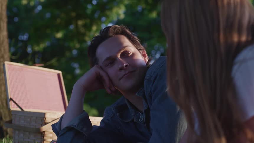 A man looks up at his girlfriend as they lie on their stomachs outside during a picnic