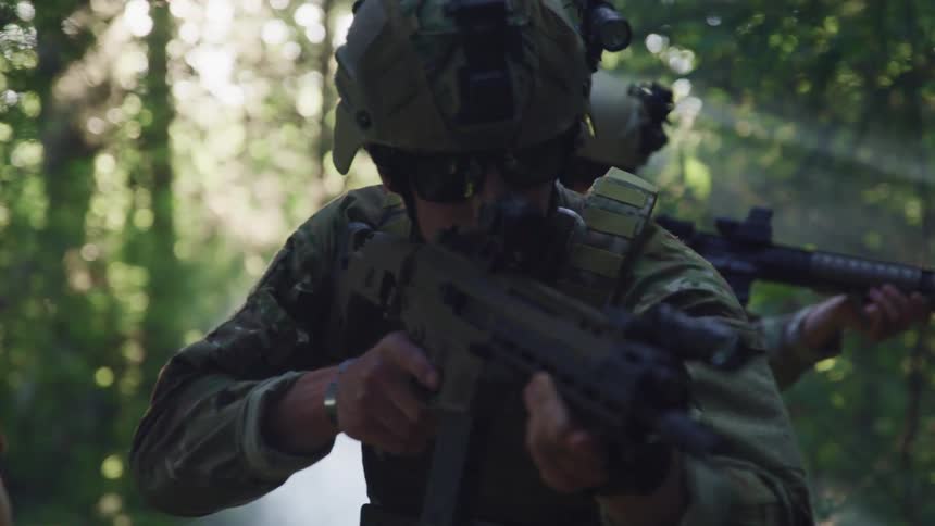 A group of people dressed in military uniforms hold guns and walk through a forest