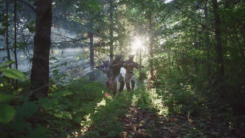 Three military men are walking through a forest at dusk