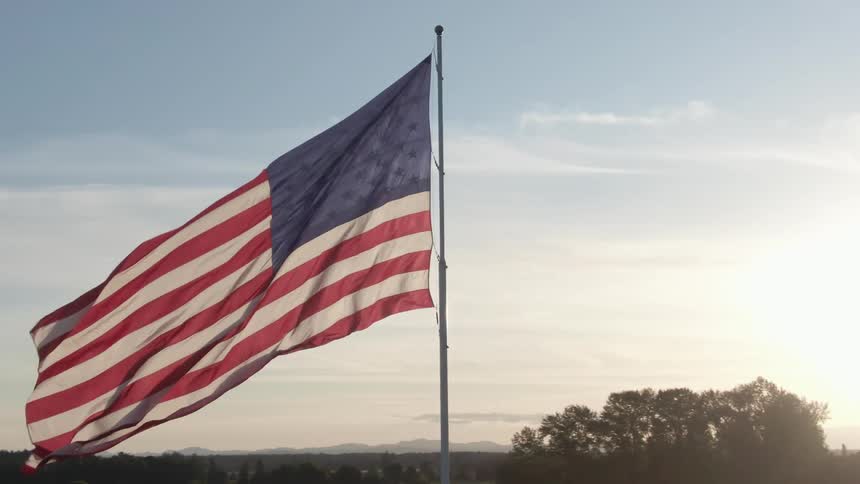 American flag on a pole fluttering in the wind on a cloudy sunny day