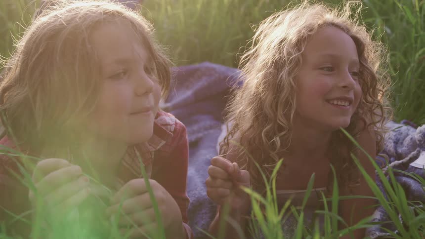 Two kids laying on the grass playing with the plants