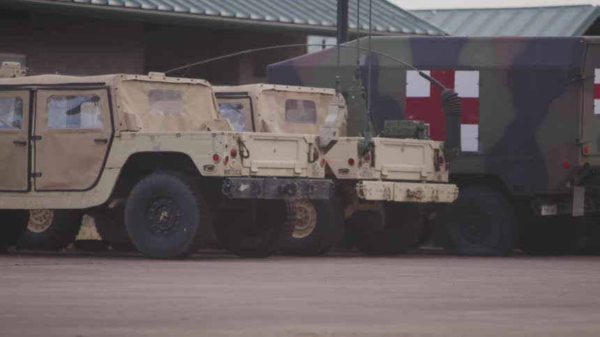 Military humvees and red cross trucks parked outside a building at evening