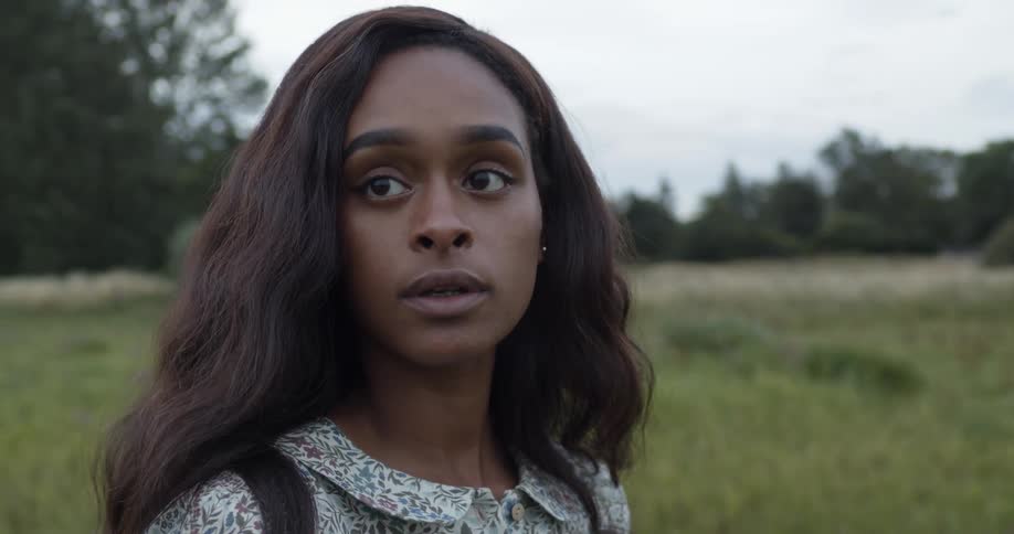 A woman in a field pushes her hair behind her ear and looks around