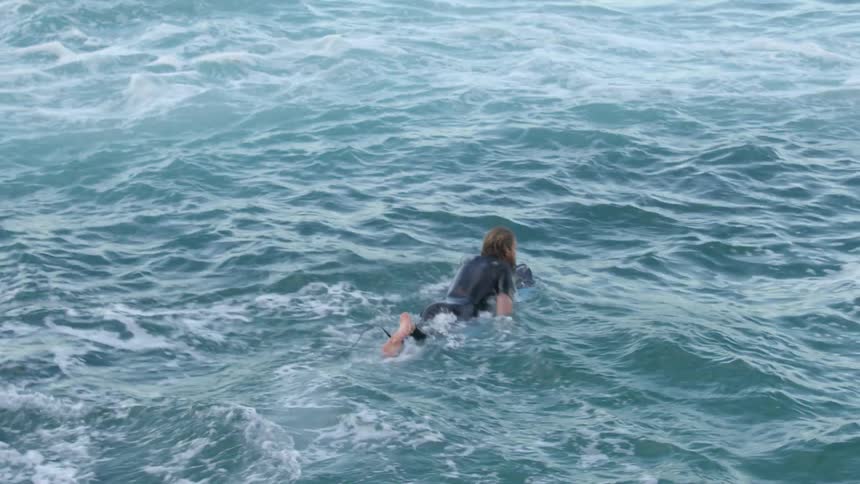 A person jumps into the ocean and paddles on a surfboard