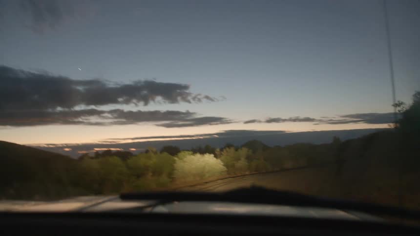 Vehicle with headlights on driving on a rural road at evening