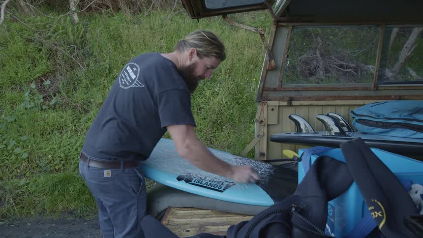 A man standing in the back of a vehicle wiping a surfboard