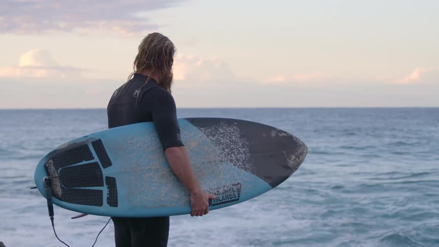 A man holding his surf board looks at the waves and walks towards the water