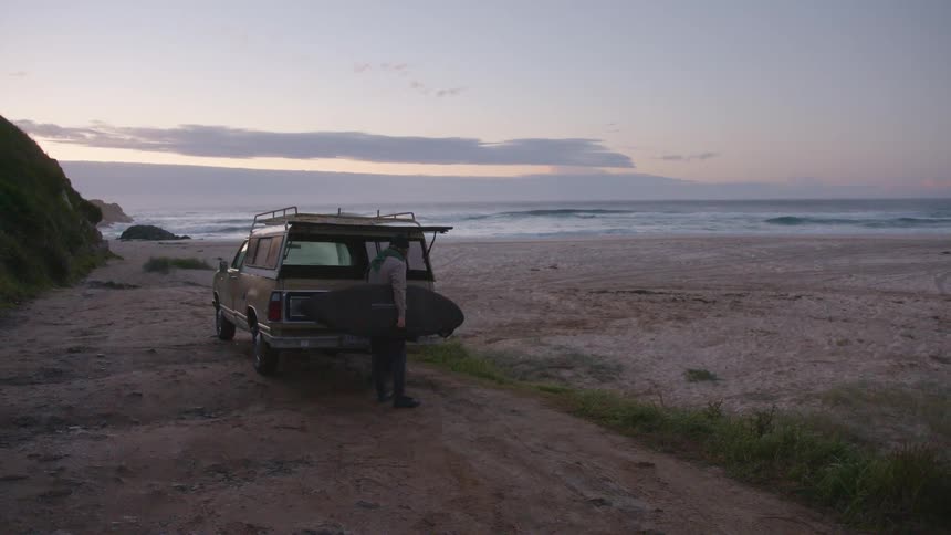 A man removes a surfboard from his truck on the beach