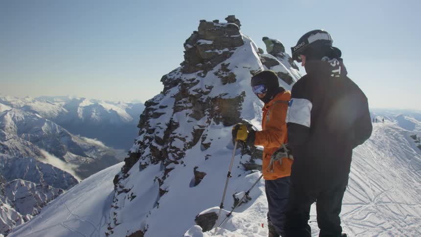 Two hikers stand on a snowy mountain and look down the snowy mountain side