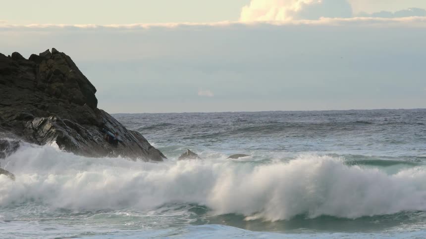 Waves rolling in rocky coast and splashing on a cloudy day