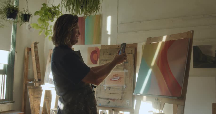 Painter wearing an apron taking a picture of his painting on his cellphone