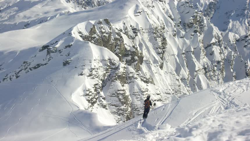 A person is standing on a snowcovered mountains looking in the direction of a valley