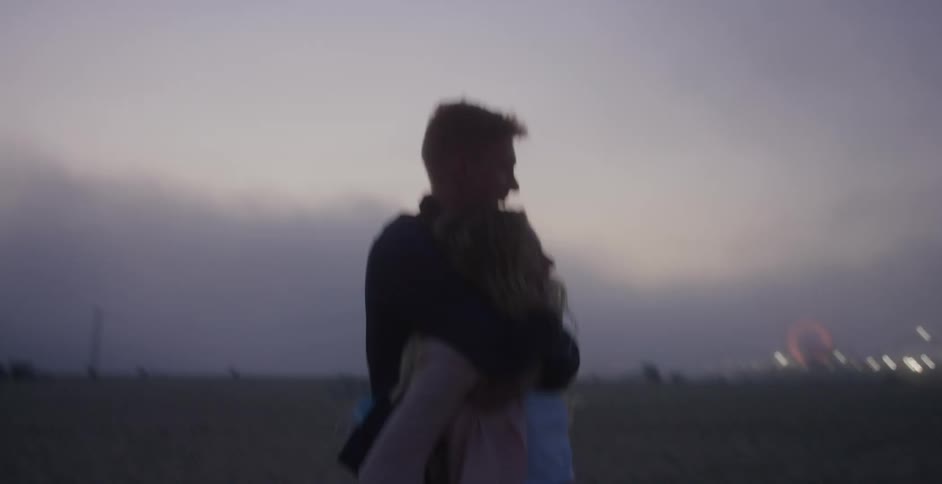 A woman carries her boyfriend on her back as they walk down a path next to the beach in the evening