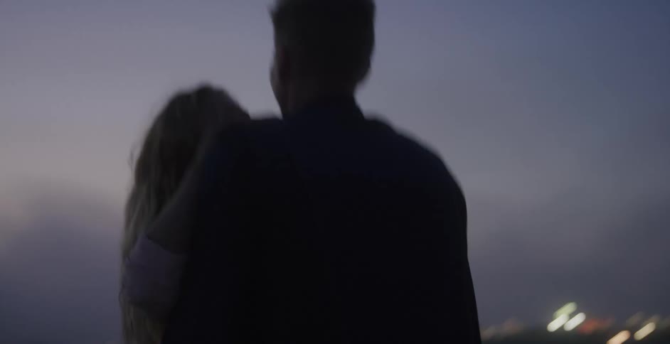 A man holds a woman in a hug and then walks off outdoors at night