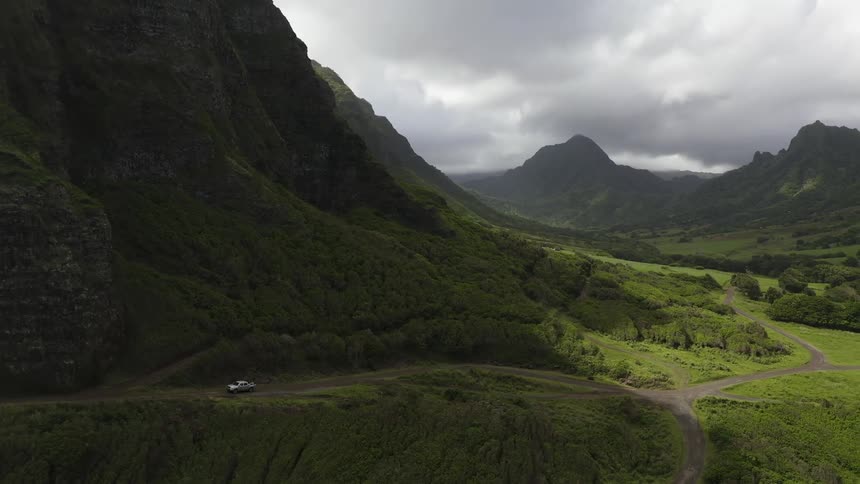 Mountain range covered with green fresh plants with winding roads and a car driving by down below at daytime