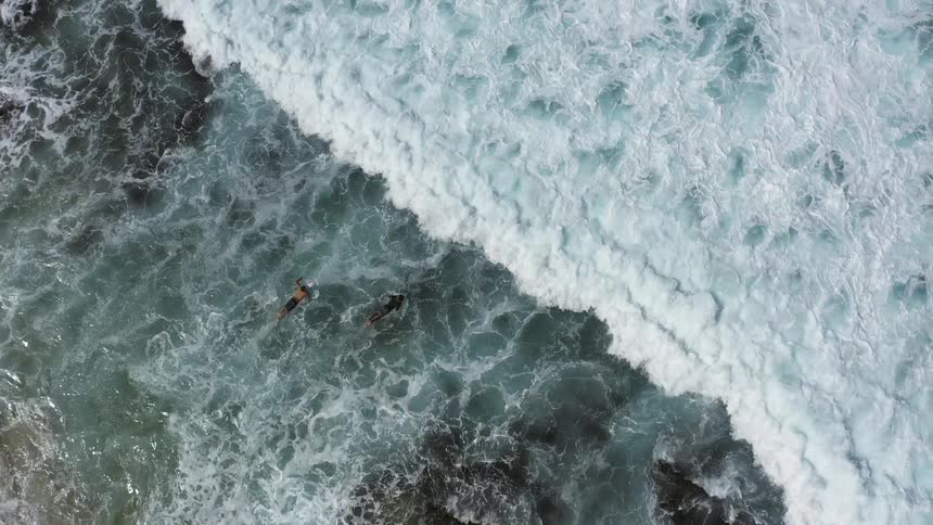 Two people swimming and surfing in the ocean next to the coast