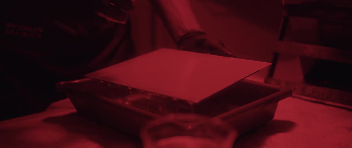 Photographer treating a sheet of glass with chemicals to develop a picture in a dark room