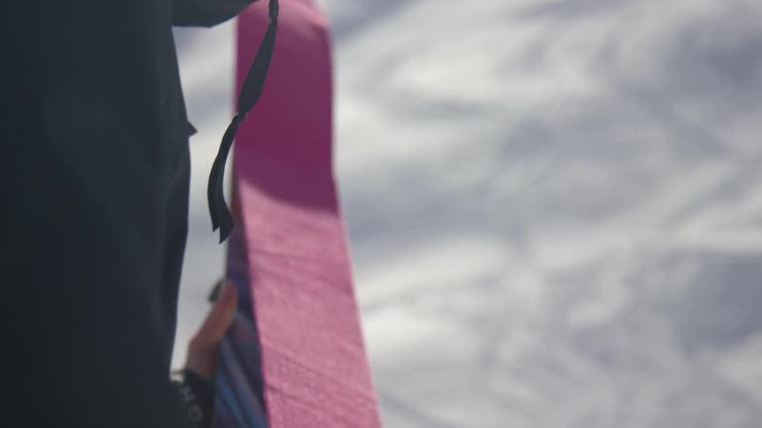 A man places a red strip of cloth across a snowboard during the day
