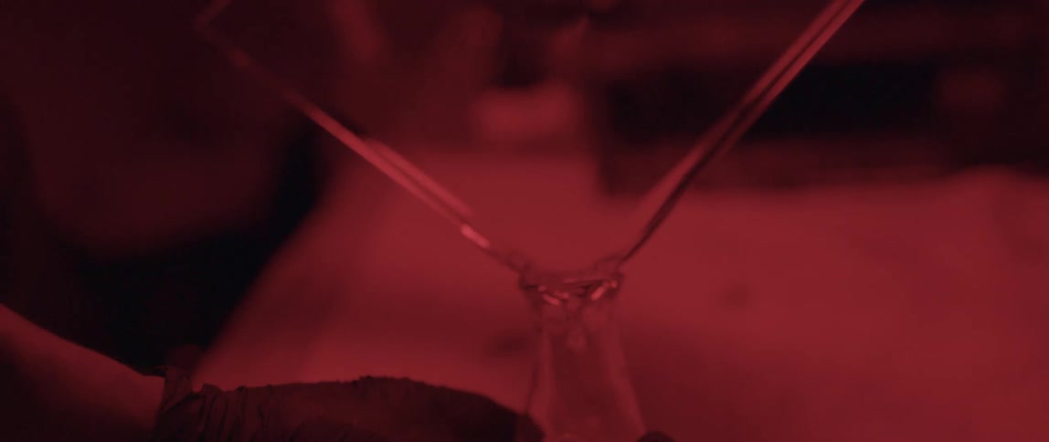 Person wearing latex gloves pouring a clear liquid off the edge of a rectangular flat piece of glass into a bottle