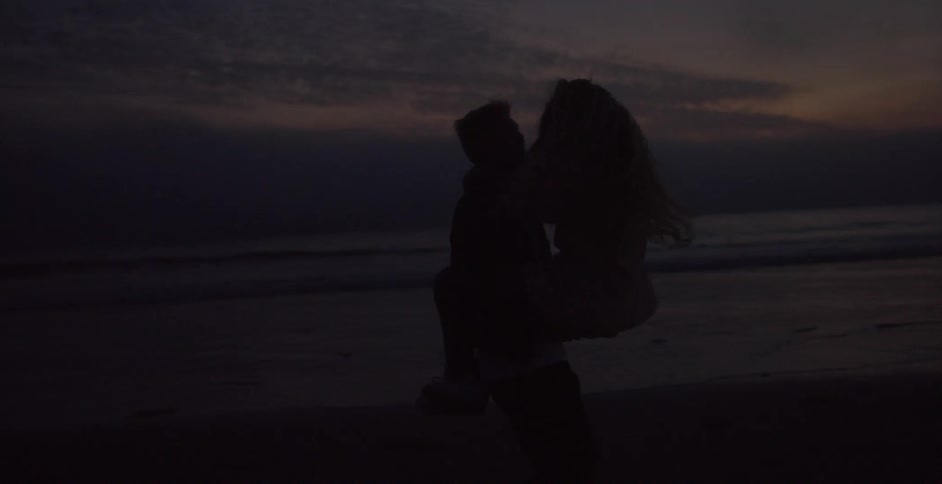 A woman on a beach at night jumps up in to a mans arms and he spins her around