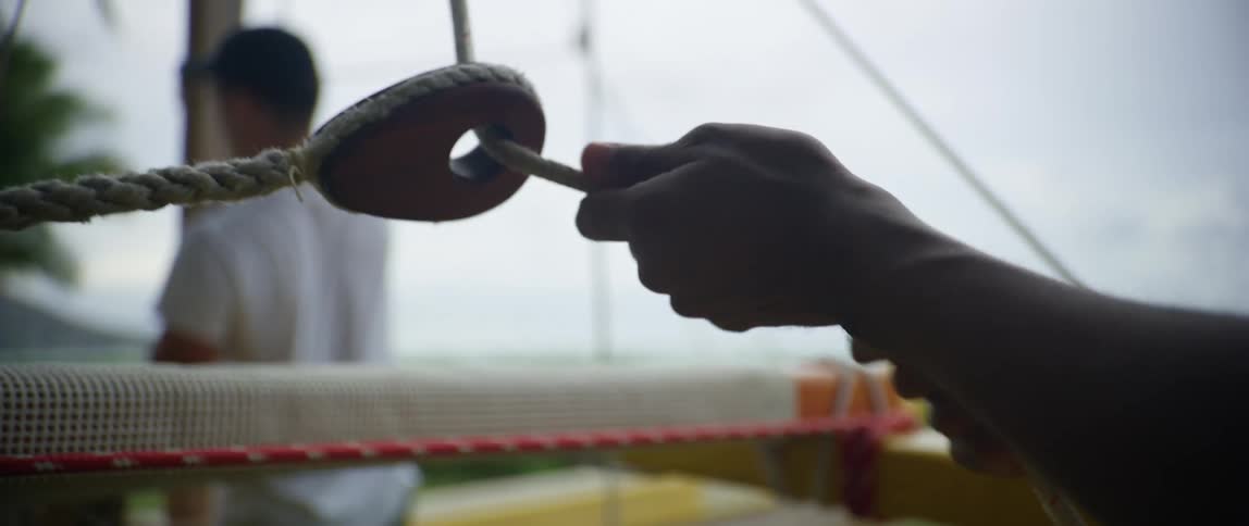 Two men pull the ropes on the ship sails