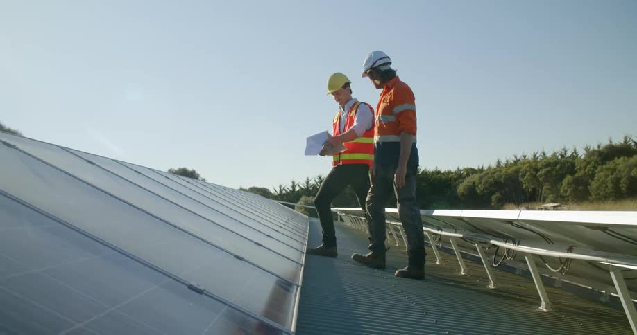 A pair of male construction workers supervising solar panels on the roof of a building