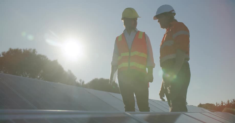 A pair of male construction workers supervising the instalation of solar panels on the roof of a building