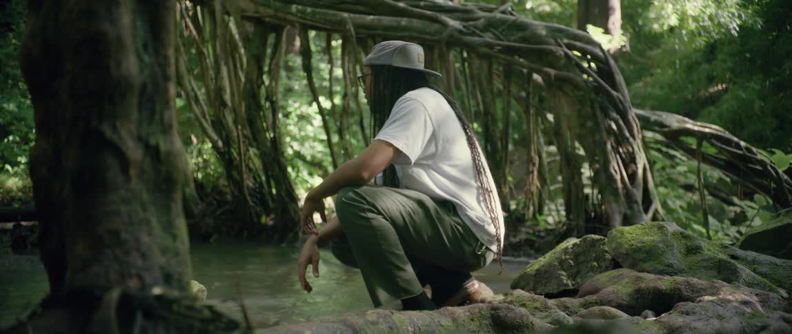 Man crouching near a river throught a tropical forest at day time