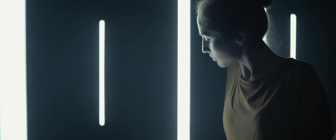 Woman dancing slowly looks up and then back down inside of a room with small lights