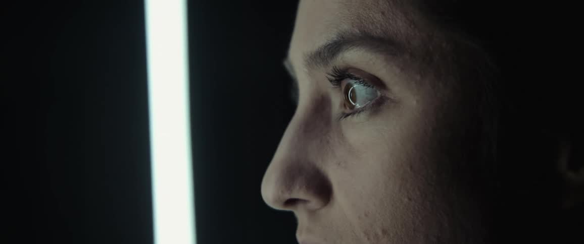 Close up of a womans face in front of a floating fluorescent lightbulb in a dark room