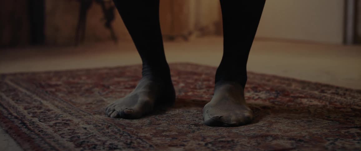 A woman standing on a rug in dirty black tights jumps and starts dancing